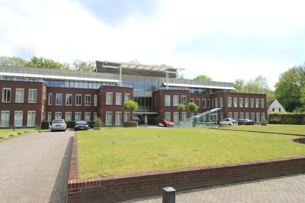 Modern kantoorgebouw aan de Arnhemse Bovenweg met glazen entree, rode bakstenen gevel en geparkeerde auto's op de oprijlaan.
